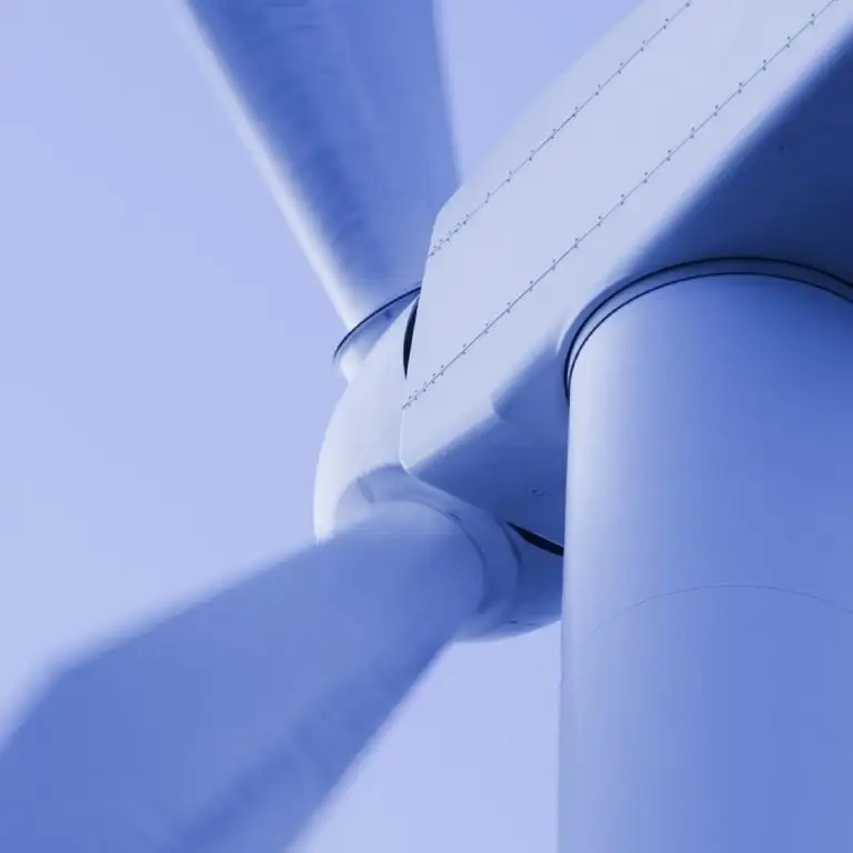 Windkraftanlage von unten fotografiert, Rotorblatt und Gondel vor hellem Himmel.