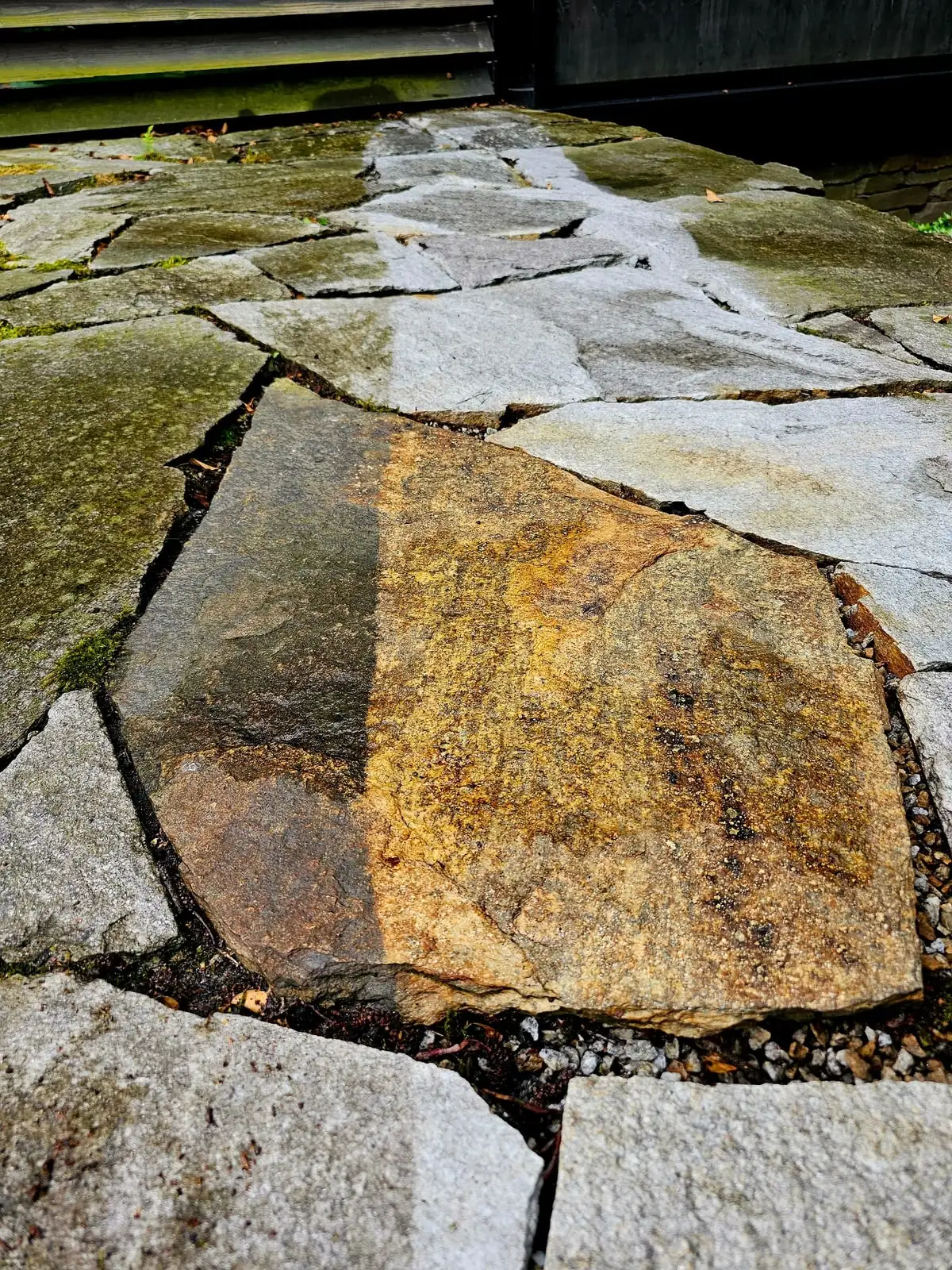 Polygonale Natursteinplatten mit deutlich sichtbarer Maserung, ein Teil der Fläche ist bereits gereinigt.