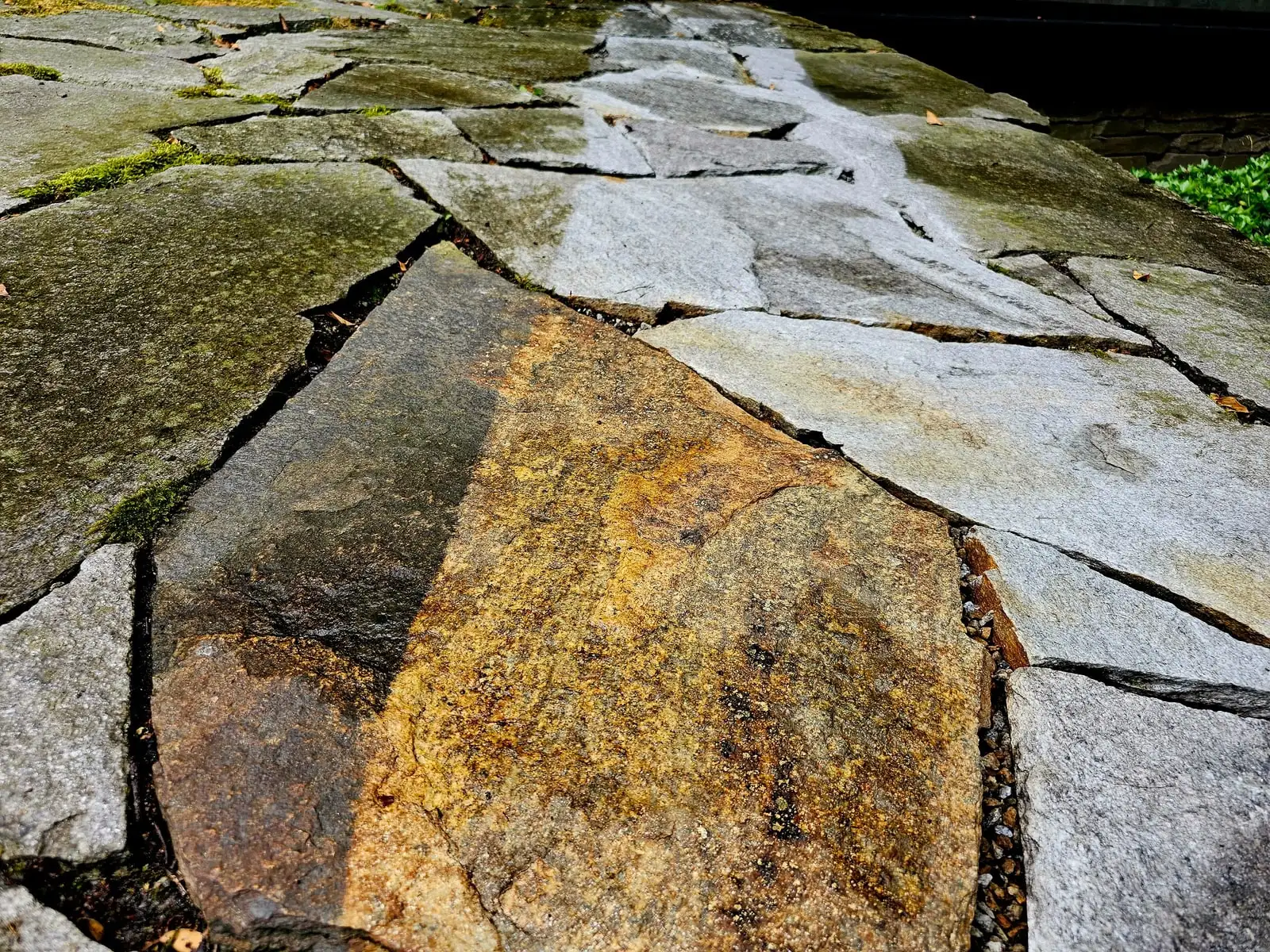 Polygonale Natursteinplatten, ein Teil gereinigt: die Maserung des Steins wird wieder sichtbar.