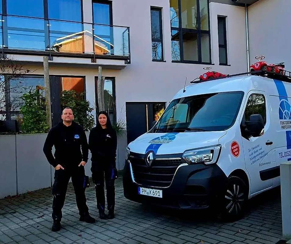Zwei Personen in dunkler Arbeitskleidung stehen auf einer gepflasterten Hoffläche neben dem beschrifteten Einsatzfahrzeug des Betriebs.